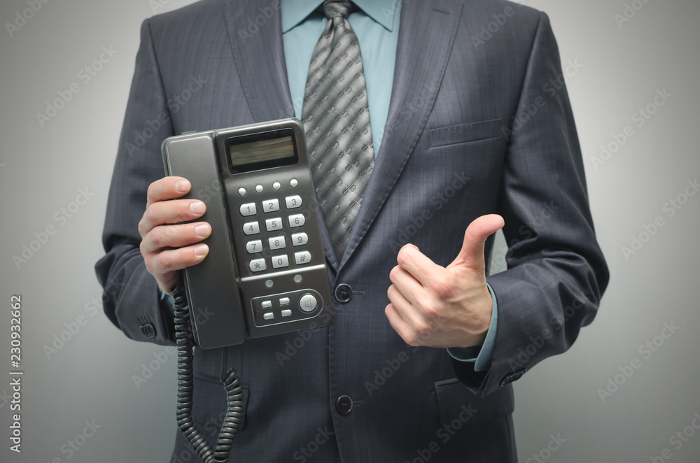 Telephone in the businessman hand isolated on the gray background. Hotline consultant.