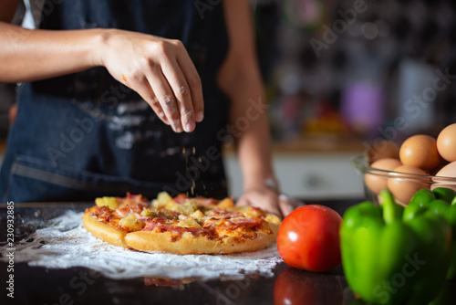 Closeup of hand female wears apron,sprinkle with flour as prepares delicious pizza, going to make surprise for family and treat with tasty pastry, Baking concept.