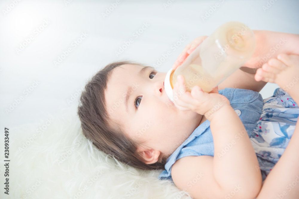 Little asian baby girl holding milk bottle and drinking by herself on bed Little asian baby girl holding milk bottle and drinking by herself on bed