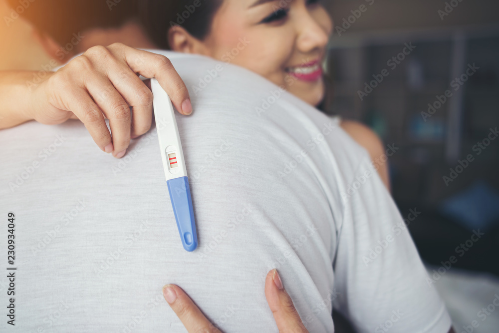 Happy couple smiling after find out positive pregnancy test in bedroom
