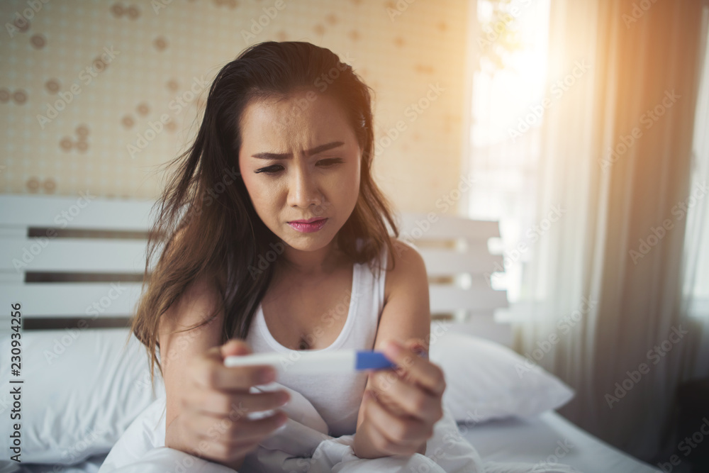Sad woman complaining holding a pregnancy test sitting on bed Sad woman complaining holding a pregnancy test sitting on bed