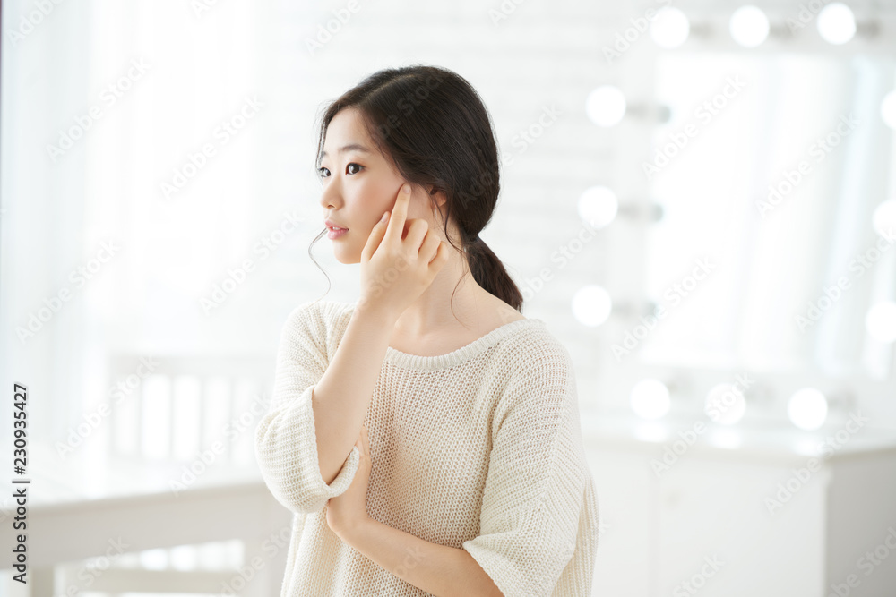 Beautiful Korean girl touching soft skin of her face with finger