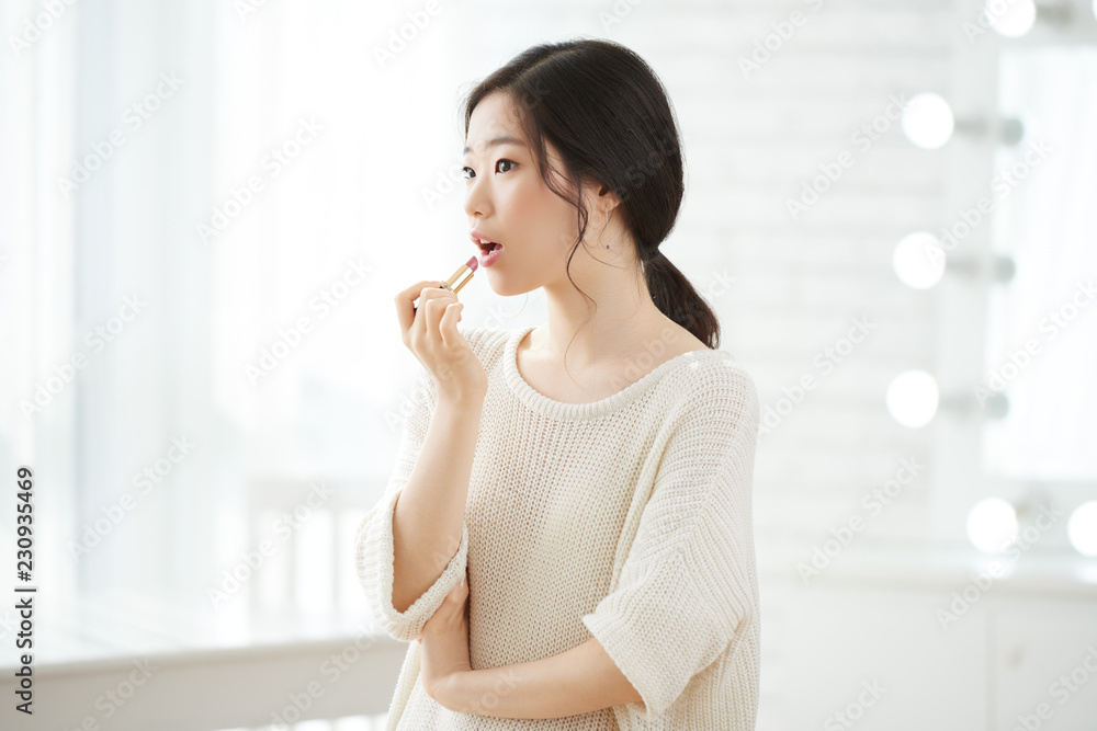 Pretty young Kirean woman applying pink lipstick Pretty young Kirean woman applying pink lipstick