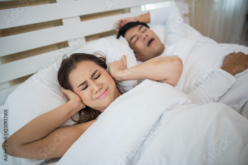 Portrait of woman blocking ears with man sleeping snoring on bed