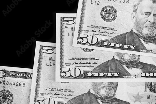 A pack of fifty dollar bills on a dark background. Black and white