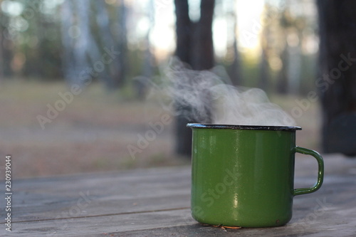 Coffee mug with steam on rough wooden table. Autumn, hiking, picnic concept. October, November, forest, hot drink