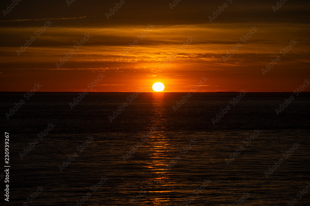 Large orange sunset as the massive sun sets into the horizon above the ocean, France