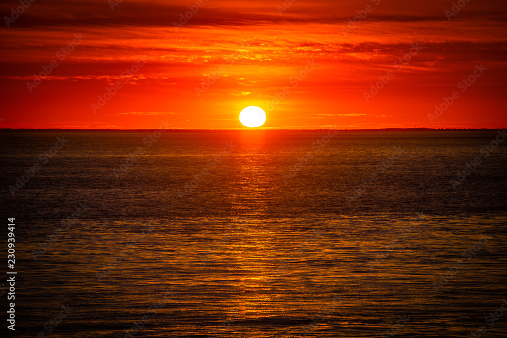 Large orange sunset as the massive sun sets into the horizon above the ocean, France