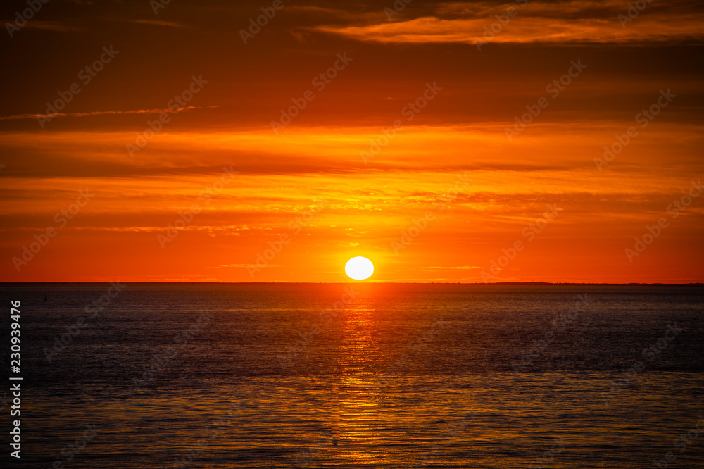 Large orange sunset as the massive sun sets into the horizon above the ocean, France