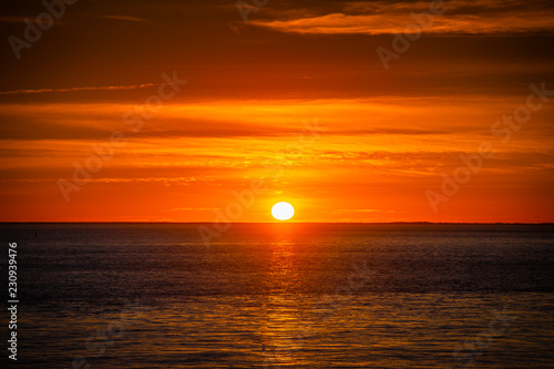 Large orange sunset as the massive sun sets into the horizon above the ocean  France