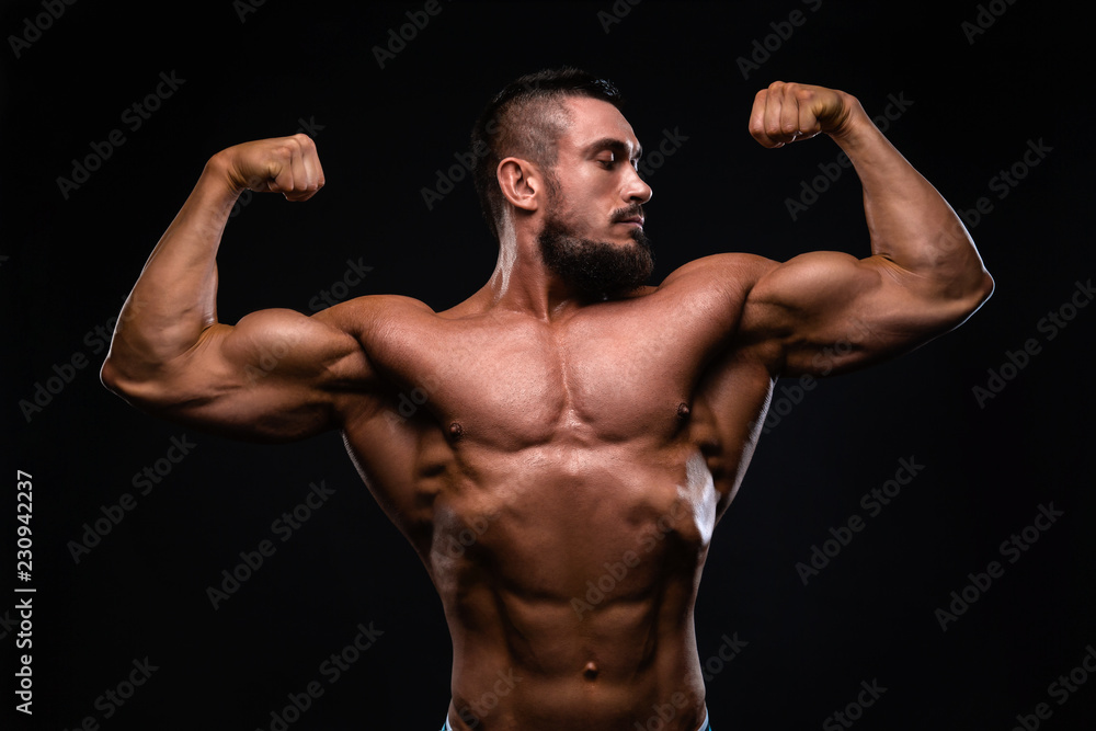 Muscular fitness burnet beard man is showing biceps on black background