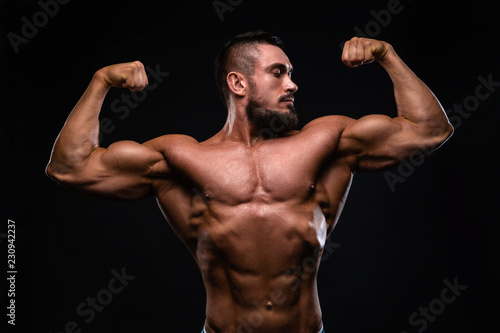 Muscular fitness burnet beard man is showing biceps on black background