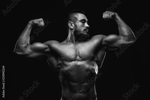 Muscular fitness burnet beard man is showing biceps on black background. BW