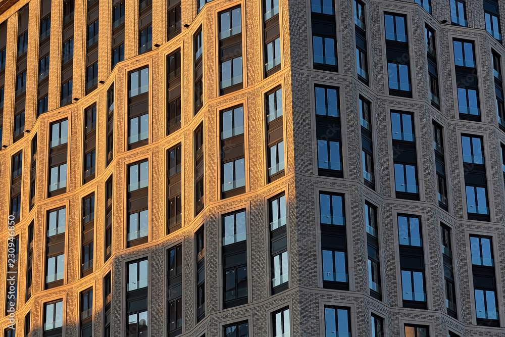 Brick wall of a skyscraper with windows. Left illuminated by sunset, right in the shade