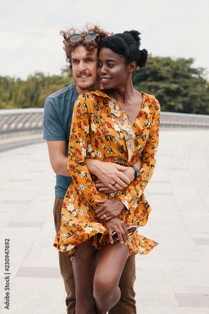 Young Caucasian man hugging his pretty African-American girlfriend from behind