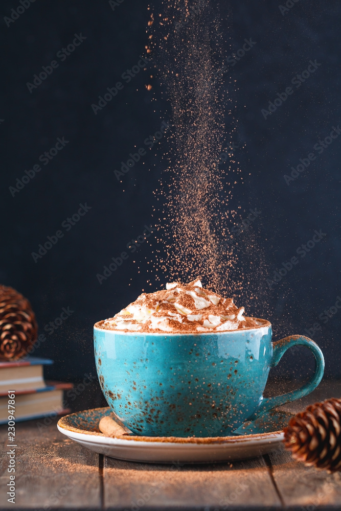 Fotobehang Chocolade Warme chocolademelk met room en kaneelstokje in een blauwe keramische beker op een tafel met boeken. Het concept van winter- of herfsttijd. #230947861