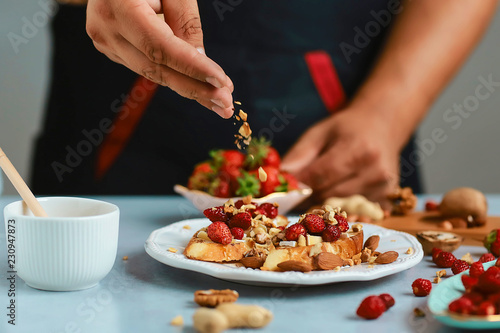 Sweet sandwiches with strawberries, cheese, camembert, brie, nuts and honey on the whole grain bread bruschetta cooking by chef hand on wooden blue light background