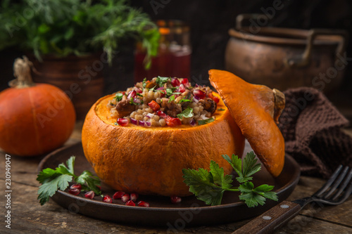 whole pumpkin stuffed with barley and vegetables, served with pomegranate and parsley photo