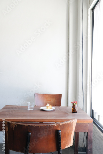 Wooden chair and wooden table with cake water on white wall background in a cafe in minimal style