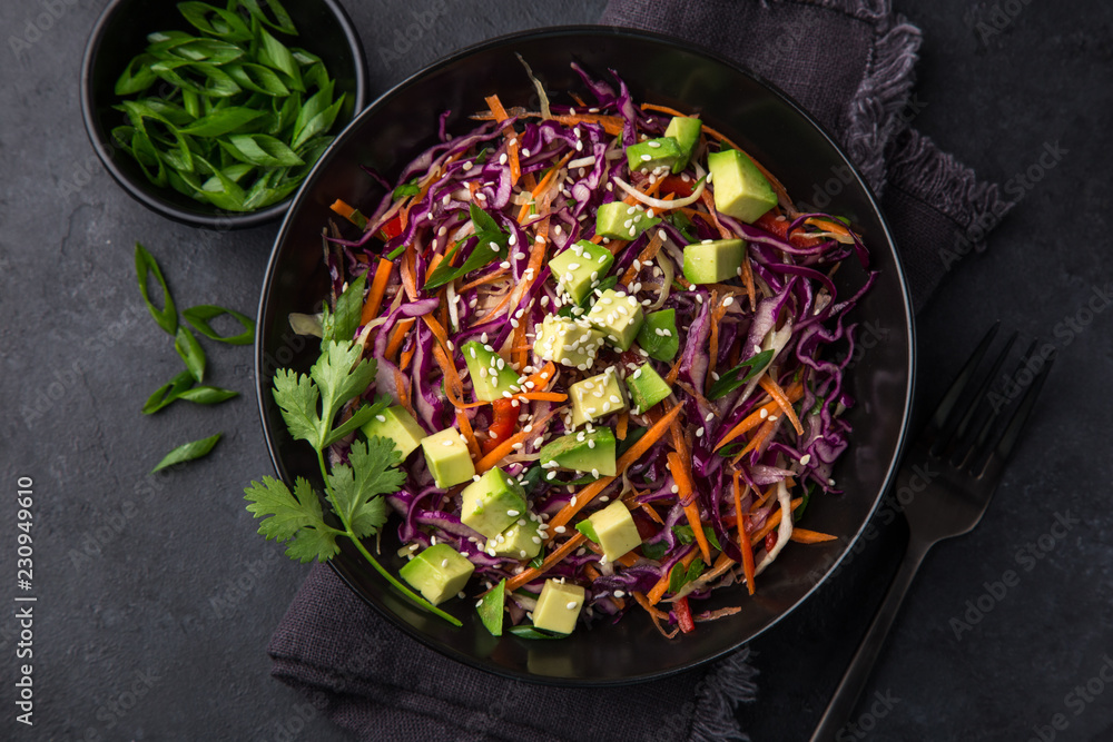 healthy rainbow cole slow, red cabbage, avocado, carrot and bell pepper salad in black bowl