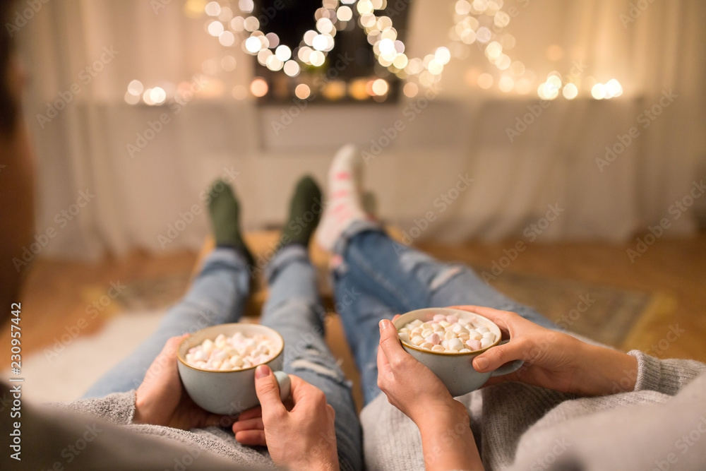 hygge, leisure and christmas concept - close up of couple drinking hot chocolate with marshmallow at home