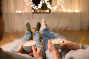 hygge, leisure and christmas concept - close up of couple drinking hot chocolate with marshmallow at home