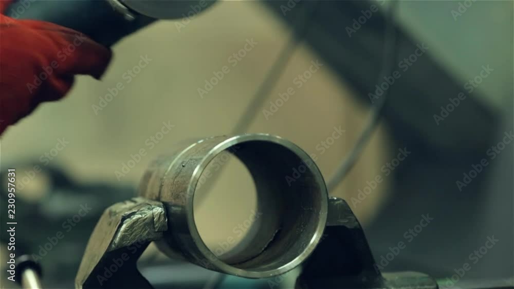 A red-gloved mechanic cleans a welded seam on a section of a steel pipe with the help of a grinding machine in the metal workshop A red-gloved mechanic cleans a welded seam on a section of a steel pipe with the help of a grinding machine in the metal workshop