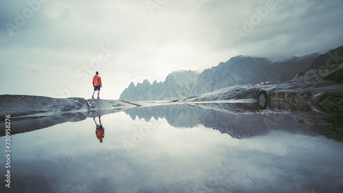  Adventurous man standing on stone. The Tungeneset rest area lies on the tip of the promontory that separates the Steinsfjord and the Ersfjord. Tungeneset Senja on the mirror refection, Norway photo