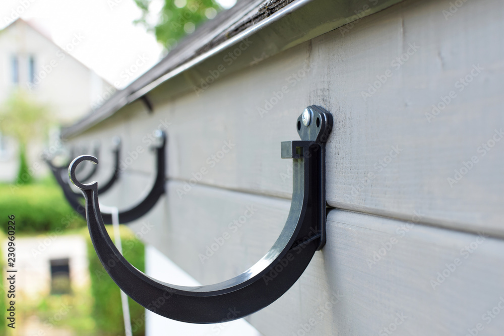 Installing black plastic rain gutter holder on wooden eaves for fixing