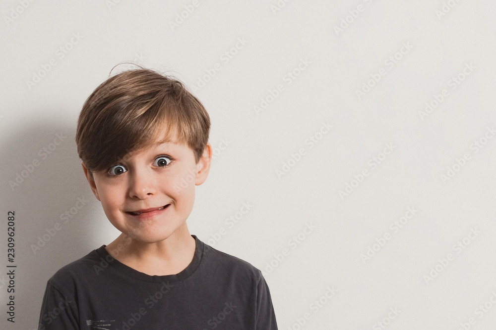 a portrait of cute boy pulling faces, dark grey shirt, white wall. Copy space for your text and design a portrait of cute boy pulling faces, dark grey shirt, white wall. Copy space for your text and design