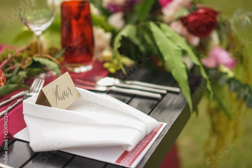 Napkin with personalized guest card on the table. Wedding dinner decor in burgundy swelling with the addition of green leaves