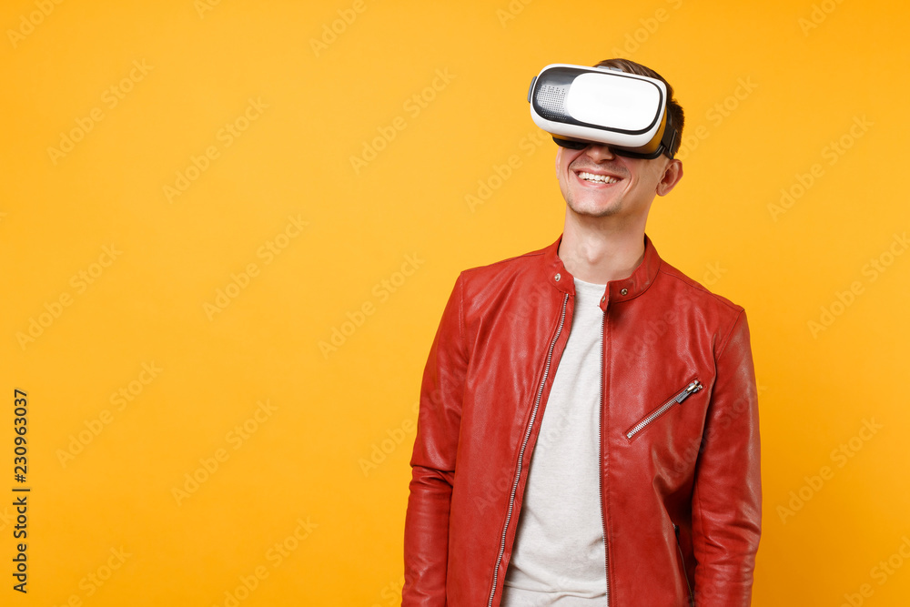 Portrait vogue handsome young man in red leather jacket, t-shirt looking in headset standing isolated on bright trending yellow background. People sincere emotions lifestyle concept. Advertising area. Portrait vogue handsome young man in red leather jacket, t-shirt looking in headset standing isolated on bright trending yellow background. People sincere emotions lifestyle concept. Advertising area.
