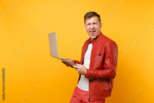 Portrait vogue fun handsome young man in red leather jacket, t-shirt using laptop pc tablet isolated on bright trending yellow background. People sincere emotions lifestyle concept. Advertising area.