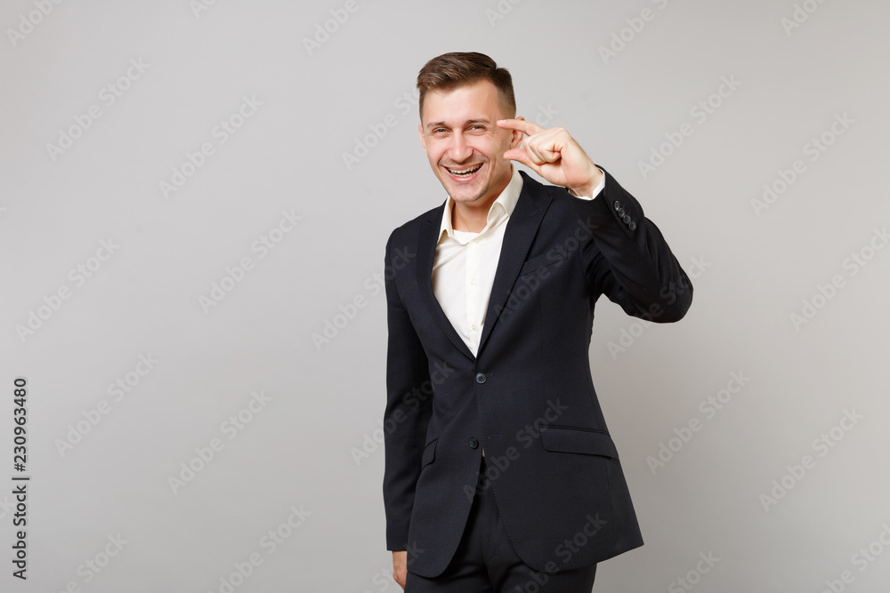 Laughing young business man in classic black suit, shirt gesturing demonstrating size with copy space isolated on grey wall background. Achievement career wealth business concept. Advertising area. Laughing young business man in classic black suit, shirt gesturing demonstrating size with copy space isolated on grey wall background. Achievement career wealth business concept. Advertising area.