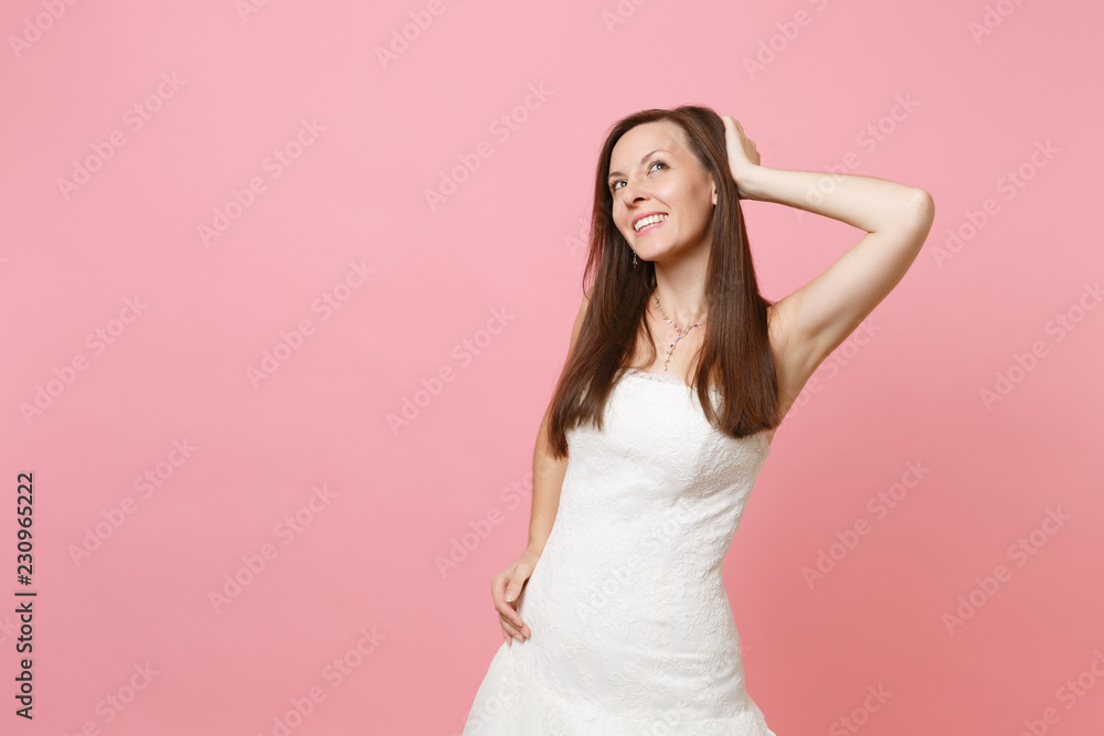 Portrait of tender bride woman in white wedding dress standing dreaming looking up keeping hand near head isolated on pink pastel background. Wedding celebration concept. Copy space for advertisement. Portrait of tender bride woman in white wedding dress standing dreaming looking up keeping hand near head isolated on pink pastel background. Wedding celebration concept. Copy space for advertisement.