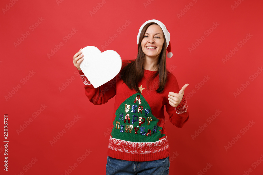 Joyful young Santa girl in Christmas hat showing thumb up, holding white blank empty heart isolated on bright red background. Happy New Year 2019 celebration holiday party concept. Mock up copy space. Joyful young Santa girl in Christmas hat showing thumb up, holding white blank empty heart isolated on bright red background. Happy New Year 2019 celebration holiday party concept. Mock up copy space.