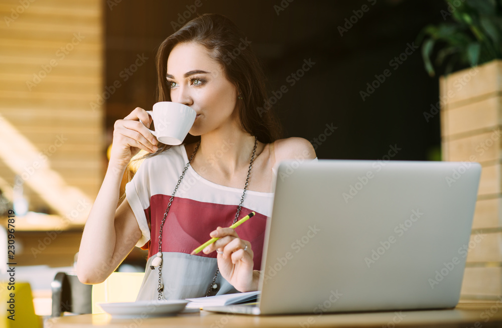 Beautiful girl working out a plan of the project and concept. Girl paints a website design on a laptop. student prints a message on the phone in the messenger. Development. Digital marketing