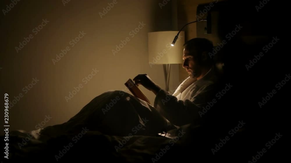 A guy reads a book under a lamp A guy reads a book under a lamp