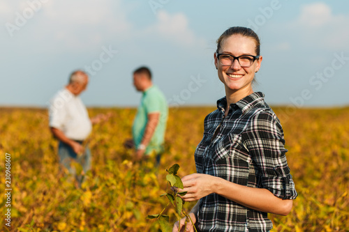 Group of farmers standing in a field examining soybean crop before harvesting. Young female farmer looking at camera.