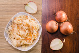 Salad of sauerkraut and carrots in a white plate and several onion bulbs on a wooden table