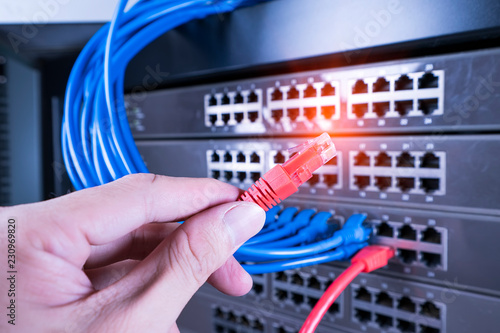 hand holding network cable on the switch hub in server room background © xiaoliangge