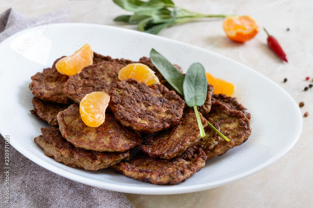 Tasty liver cutlets with tangerines on a white plate on the table.