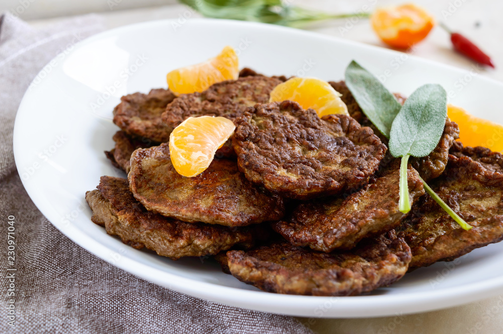 Tasty liver cutlets with tangerines on a white plate on the table.
