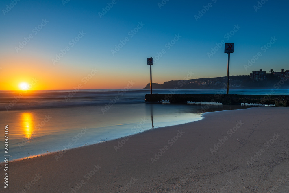 Sunrise over iconic Manly Beach, Sydney Australia. Clear skies and the storm water pipes lead the long exposure image.