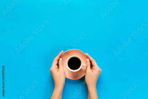 female arms hold mug of coffee on blue background. top view with cope space