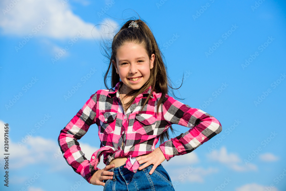 Child cute girl long hair ponytail hair. Fashion model girl. Stylish fashionable kid. Kids fashion concept. Kid girl checkered fashionable shirt posing sunny day blue sky background Child cute girl long hair ponytail hair. Fashion model girl. Stylish fashionable kid. Kids fashion concept. Kid girl checkered fashionable shirt posing sunny day blue sky background