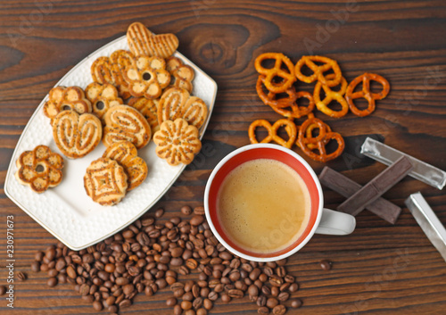 A cup of coffee, grains of coffee and cookies on a wooden table.