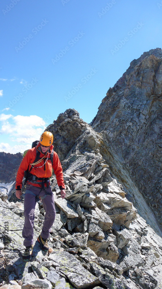 mountain climber hiking along a sharp and rocky mountain ridge under a blue sky