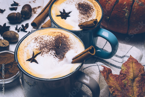 Pumpkin spice latte or coffee with cinnamon and nutmeg. Autumn, fall or winter hot drink. Old white wooden background with yellow leaves and pumpkins