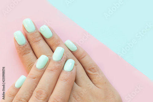 Tender hands with perfect blue manicure on trendy pastel pink background. Place for tex